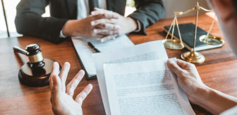 Two people discussing legal documents at a desk with a gavel and scales of justice nearby.