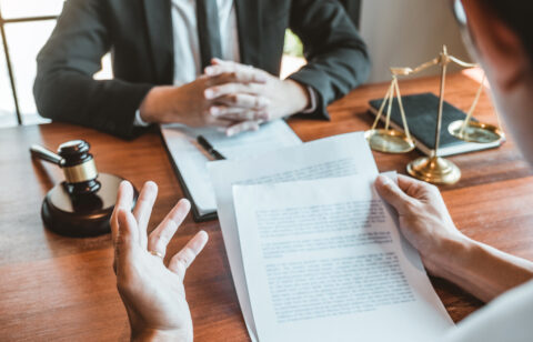 Two people discussing legal documents at a desk with a gavel and scales of justice nearby.