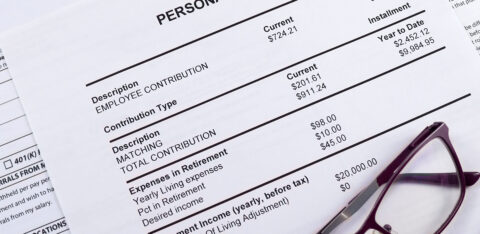 Close-up of a personal 401k plan statement showing employee contributions, matching amounts, and retirement income details, with a pair of eyeglasses resting on the paper.