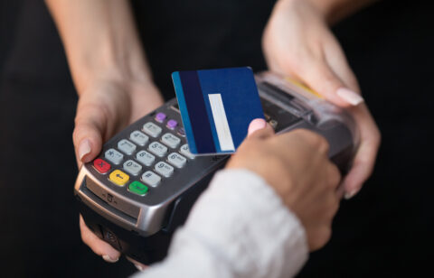 Close-up of a person swiping a blue credit card through a payment terminal held by a cashier.