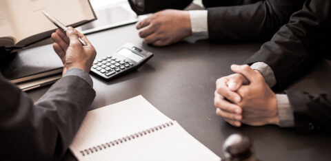 Close-up of people in suits meeting at a desk with legal documents, a calculator, and a gavel.