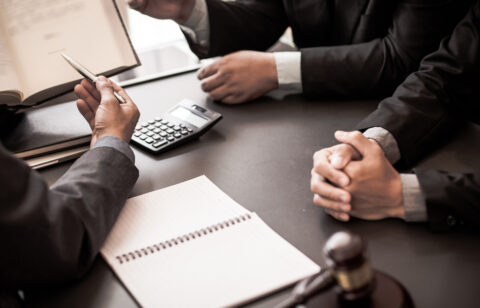 Close-up of people in suits meeting at a desk with legal documents, a calculator, and a gavel.