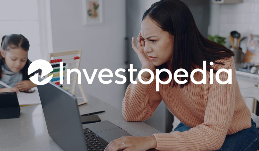 Stressed mother managing bills on her laptop with her child studying nearby, with the Investopedia logo overlayed.