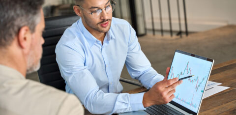 Man in glasses pointing at a financial graph on a laptop while discussing data with a colleague