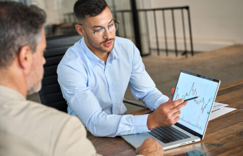 Man in glasses pointing at a financial graph on a laptop while discussing data with a colleague