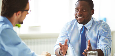 Business professional in a striped shirt speaking with a colleague during a meeting.
