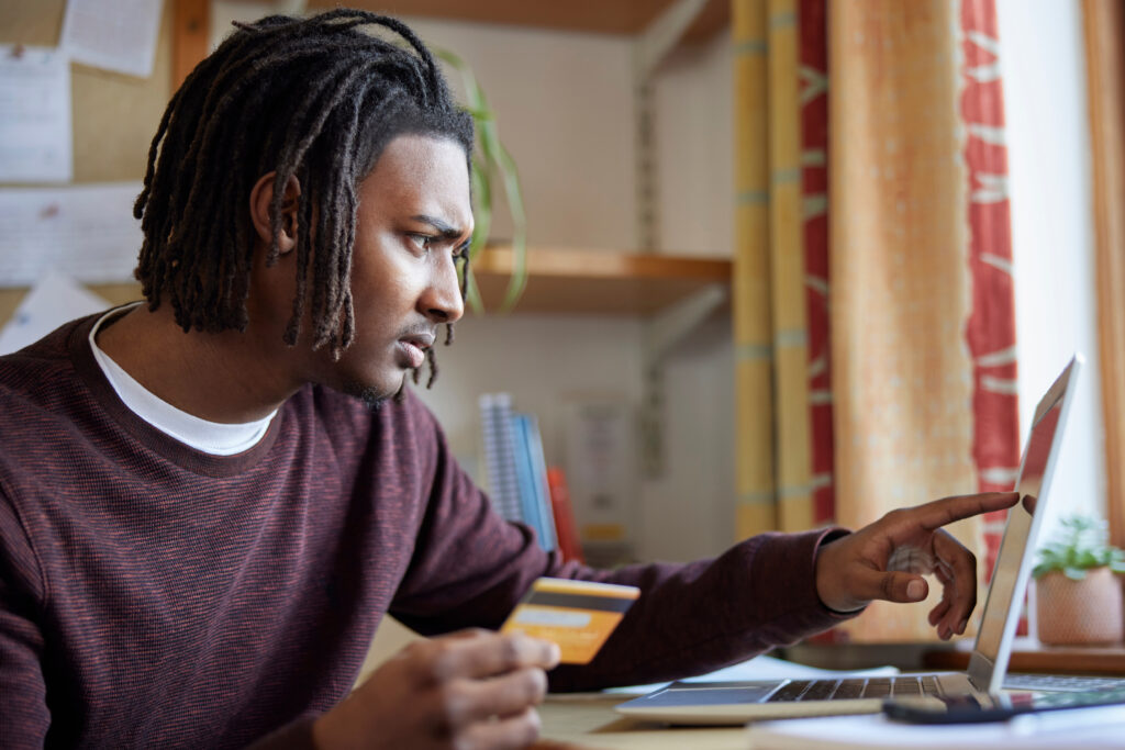 Man holding a credit card while using a laptop, focused on managing finances online.