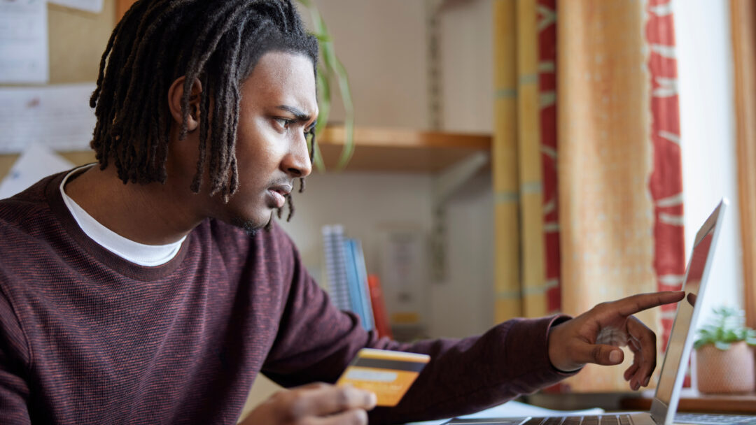 Man holding a credit card while using a laptop, focused on managing finances online.