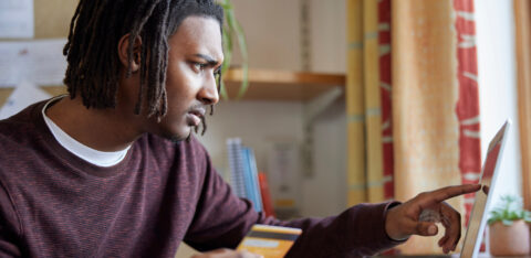 Man holding a credit card while using a laptop, focused on managing finances online.