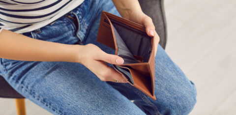 A seated person holding open an empty wallet