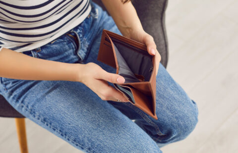 A seated person holding open an empty wallet