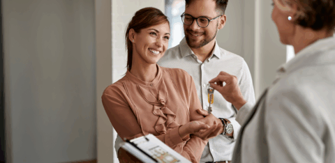 A smiling couple receives house keys from a real estate agent after buying their first home.