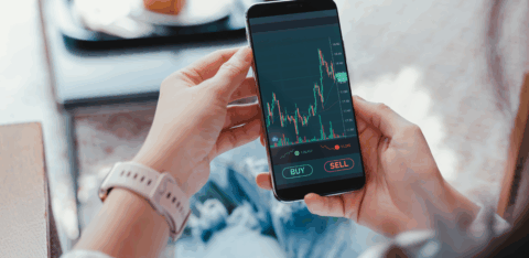 Person holding a smartphone displaying a stock trading app with buy and sell options.