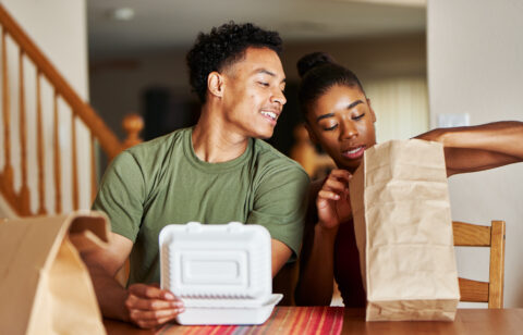 A couple sits at a dining table enjoying takeout food together at home.