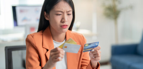 Woman looking concerned while comparing multiple credit cards at her desk.