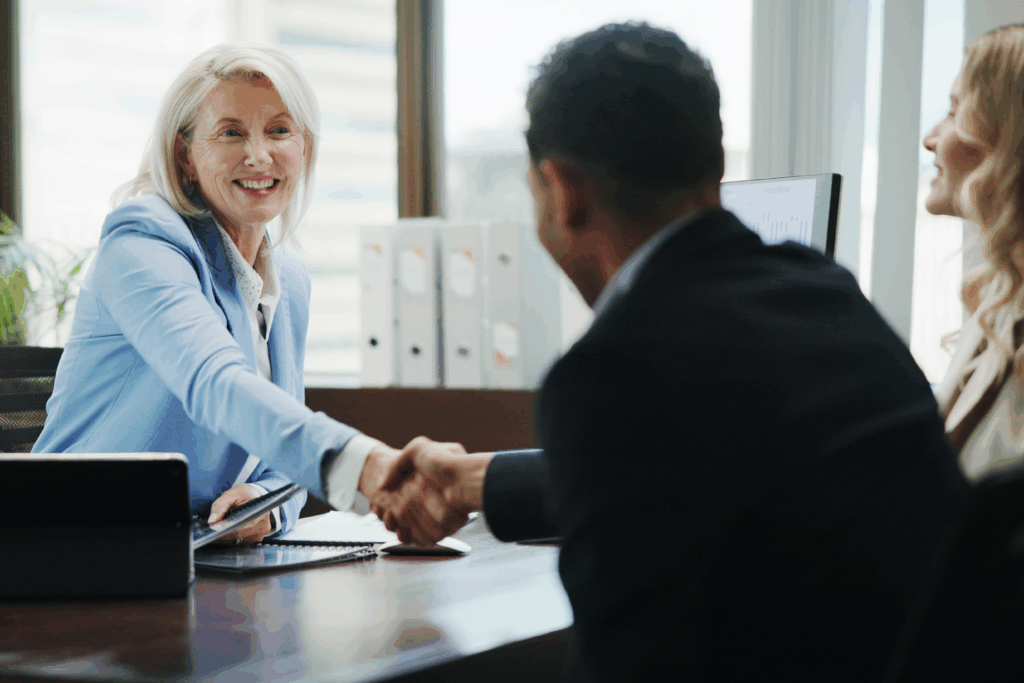 Smiling businesswoman in a meeting shaking hands with a client across a desk.