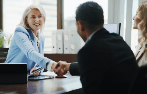 Smiling businesswoman in a meeting shaking hands with a client across a desk.