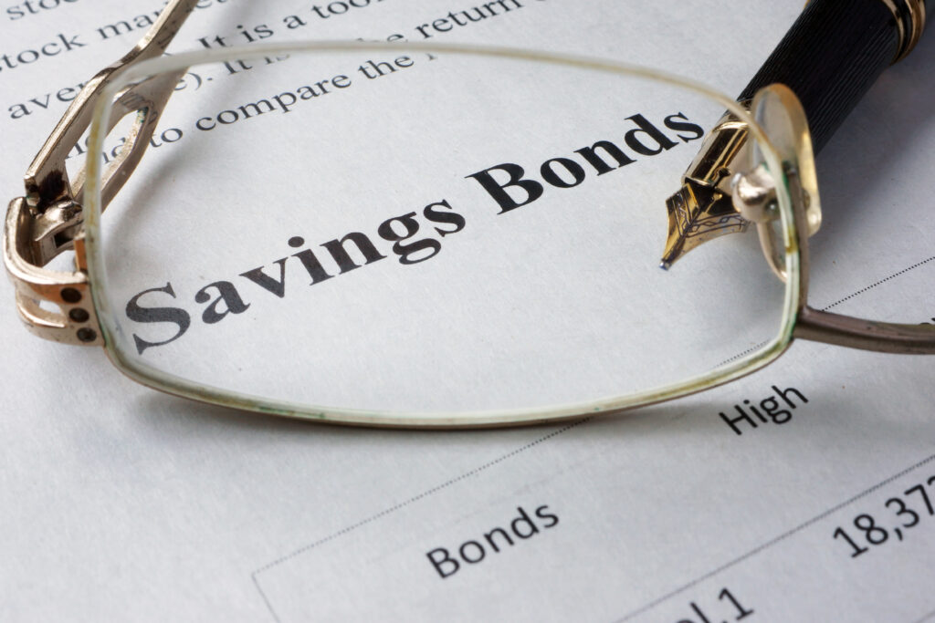 Close-up of the words "Savings Bonds" on a financial document with eyeglasses and a pen resting on the page.