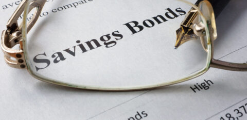 Close-up of the words "Savings Bonds" on a financial document with eyeglasses and a pen resting on the page.