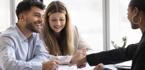 Smiling couple meeting with a professional to review and sign financial documents.