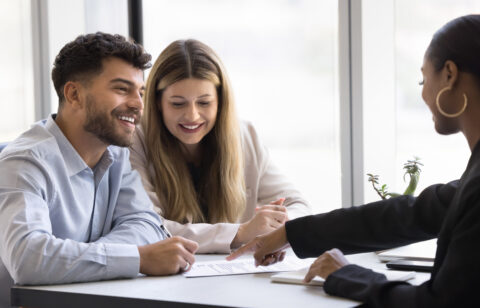 Smiling couple meeting with a professional to review and sign financial documents.