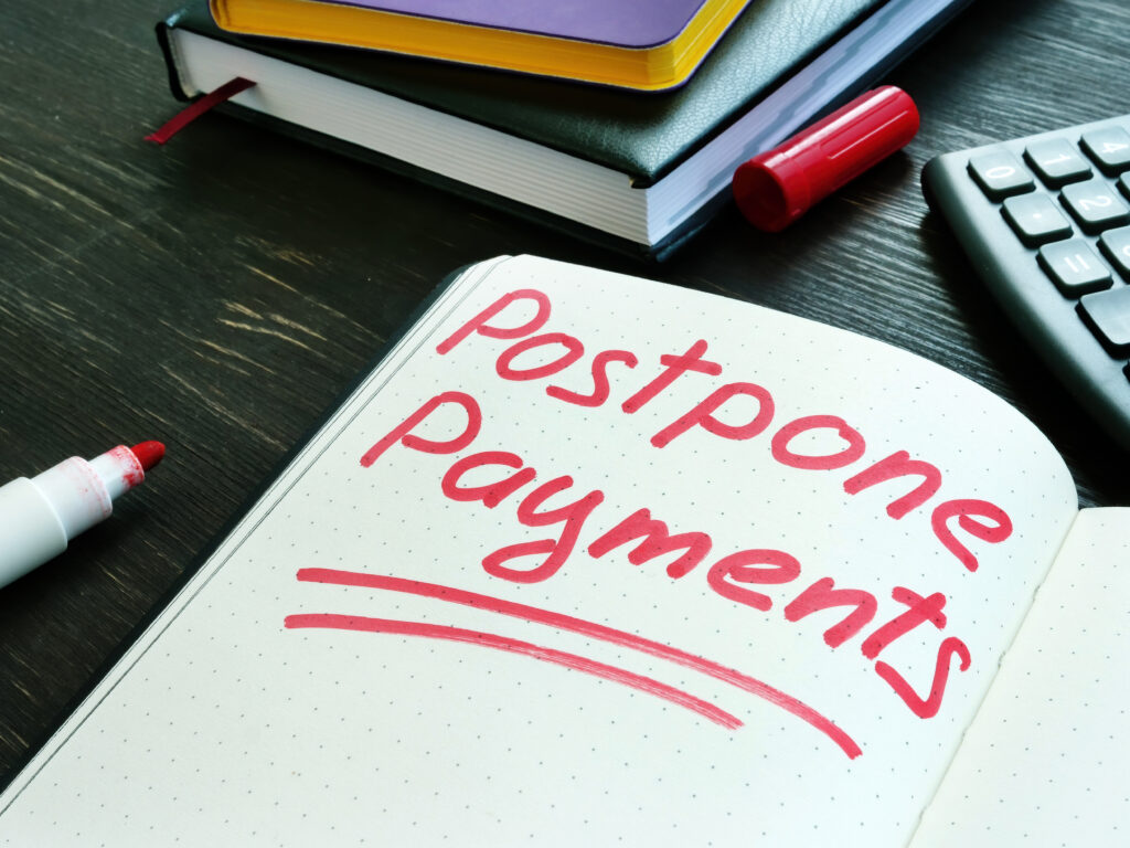 The words “postpone payments” written in red marker on an open notebook beside a calculator and books.