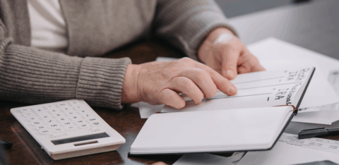 An older adult reviews notes about retirement accounts while going over financial paperwork at a table.