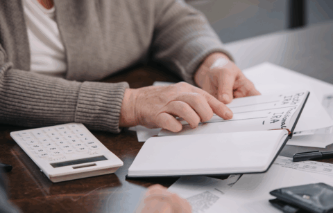 An older adult reviews notes about retirement accounts while going over financial paperwork at a table.