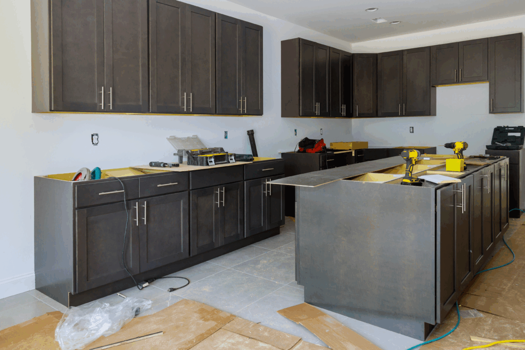 A kitchen under construction with dark cabinets, tools, and materials spread across the floor and counters.