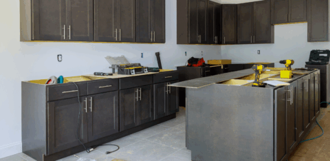 A kitchen under construction with dark cabinets, tools, and materials spread across the floor and counters.