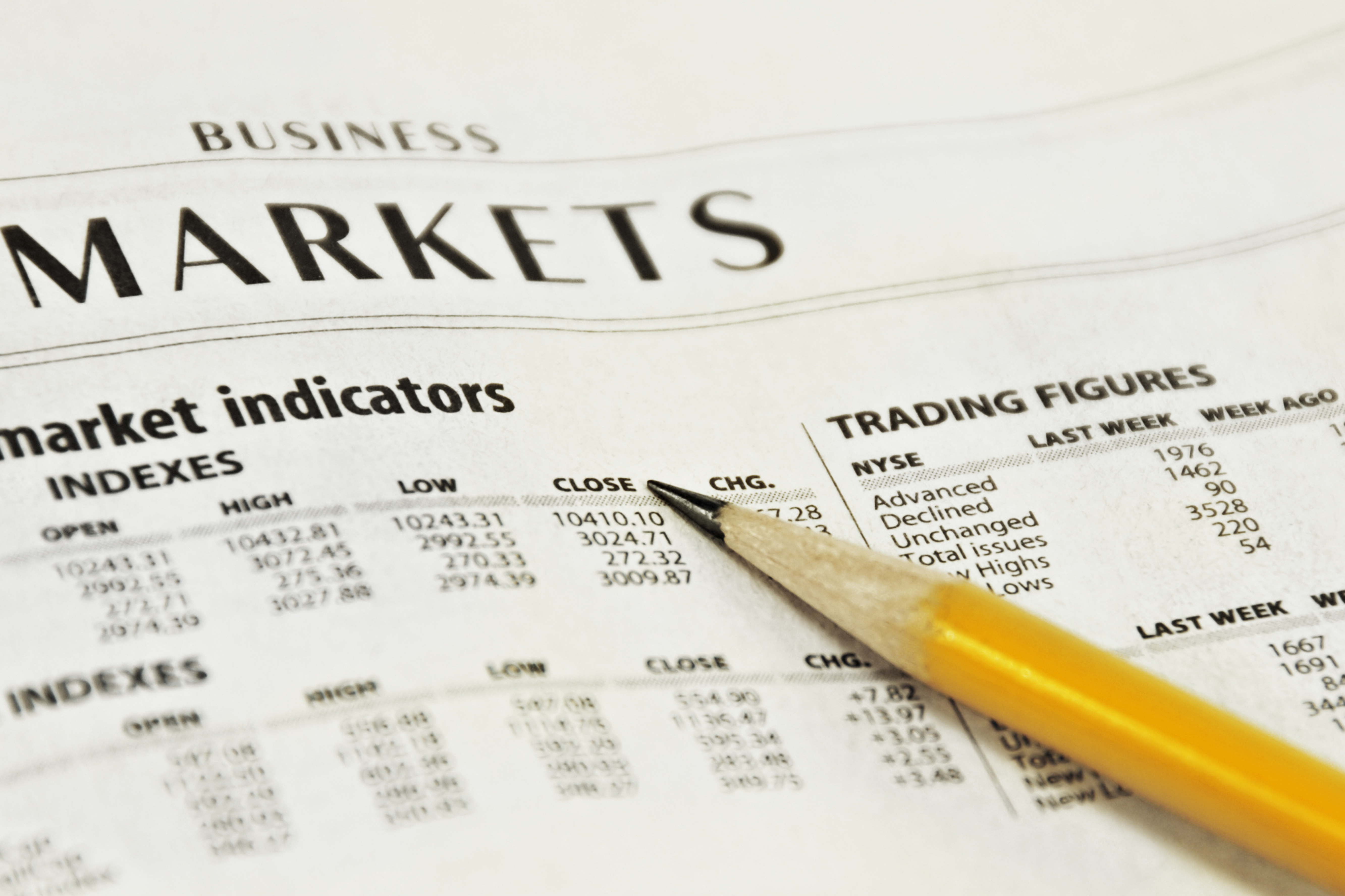 A close-up of financial tables in a newspaper with a pencil pointing toward stock market data.