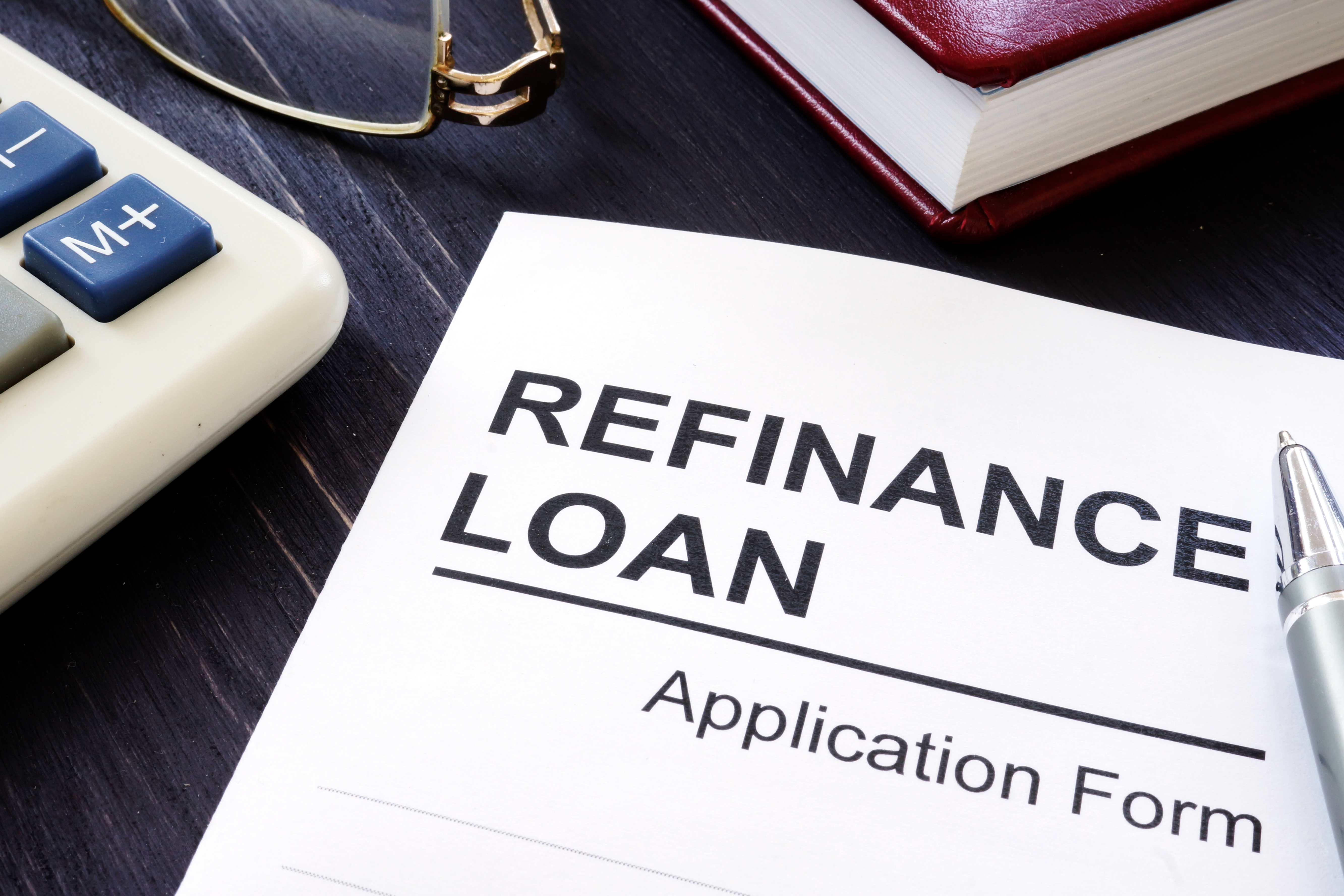 A refinance loan application form on a desk beside a calculator, glasses, and a pen.