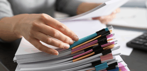 Hand organizing a large stack of documents secured with colorful binder clips on a desk.