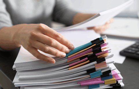 Hand organizing a large stack of documents secured with colorful binder clips on a desk.