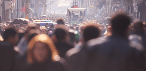 Large crowd of people walking along a busy city street with a streetcar visible in the distance.