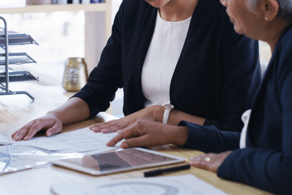 Two people reviewing paperwork together at a desk, with documents and a tablet laid out in front of them.