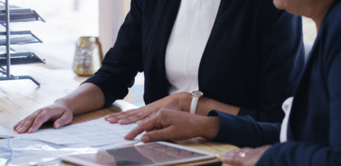 Two people reviewing paperwork together at a desk, with documents and a tablet laid out in front of them.