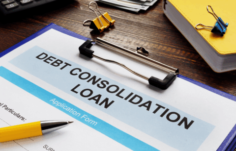 Debt consolidation loan application form on a clipboard, with a pen, calculator, cash, and office supplies on a desk.