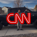 Person standing beside a large black pickup truck in a suburban driveway, with a red CNN logo overlaid on the image.