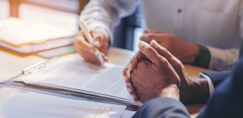 Close-up of two people reviewing and signing documents at a desk during a business meeting.