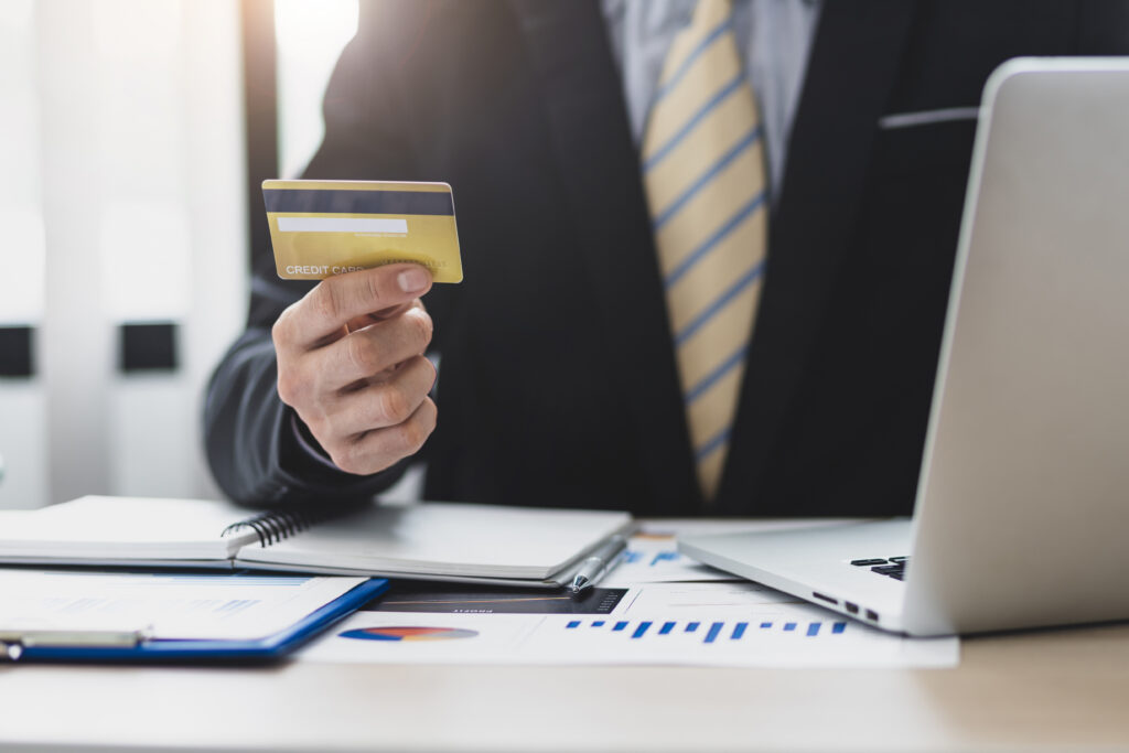 Business professional holding a credit card while sitting at a desk with a laptop and financial documents.
