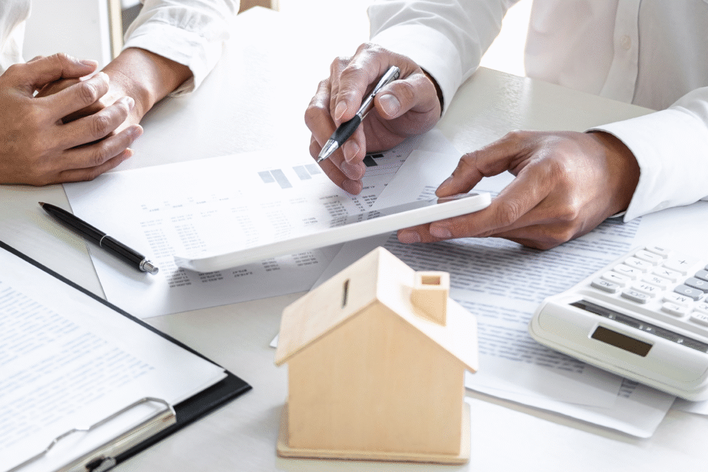 Two people reviewing financial documents with a calculator and small model house on the table.