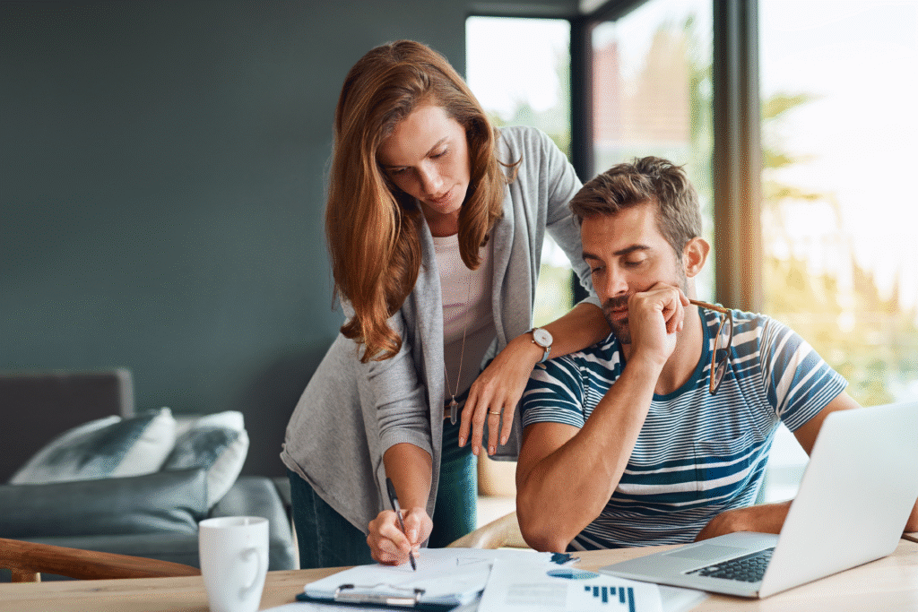 Couple reviewing financial documents at a table with a laptop and coffee mug.