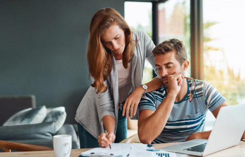 Couple reviewing financial documents at a table with a laptop and coffee mug.
