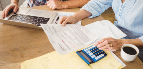 Couple reviewing financial paperwork at a table with a laptop, calculator, and coffee.
