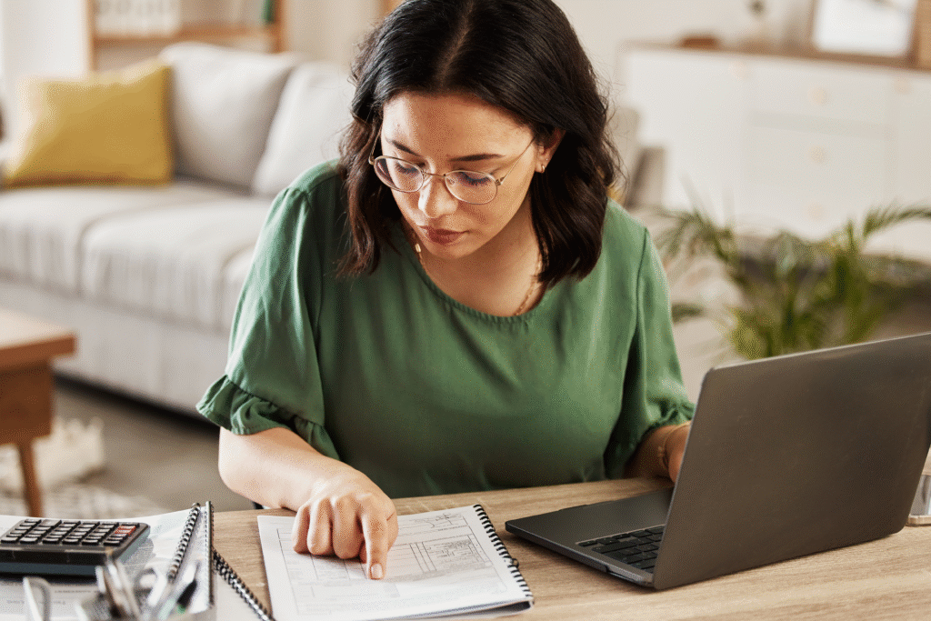 Woman reviewing paperwork at a table with a laptop and calculator.