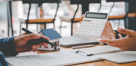 Two people reviewing financial documents with a calculator and small model house on the table.