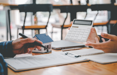 Two people reviewing financial documents with a calculator and small model house on the table.