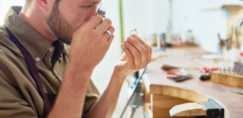 Man inspecting a ring closely using a jeweler’s loupe in a jewelry workshop.