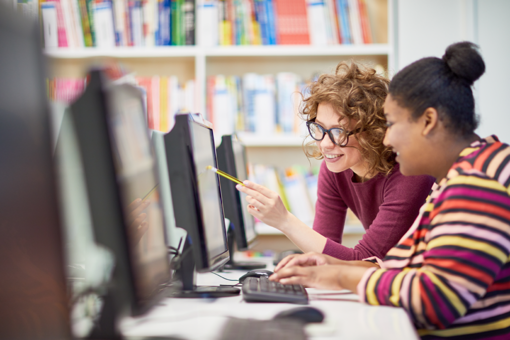 Two college students working together at a computer in a library or computer lab